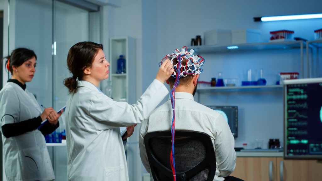 back view man patient wearing performant brainwave scanning headset sitting neurological research laboratory while medical researcher adjusting it examining nervous system