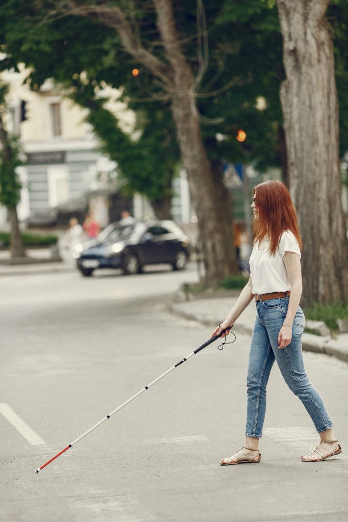 young blind person with long cane walking city